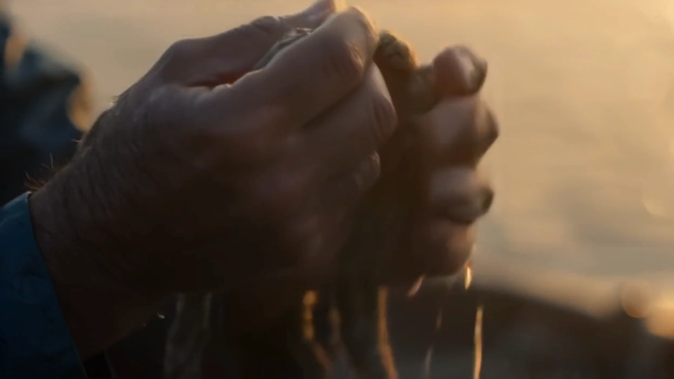 Close-up of weathered hands letting sand fall at sunset